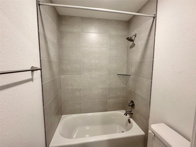bathroom with toilet, washtub / shower combination, and a textured wall