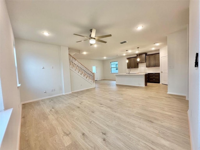 unfurnished living room featuring a ceiling fan, stairway, light wood-style flooring, baseboards, and recessed lighting
