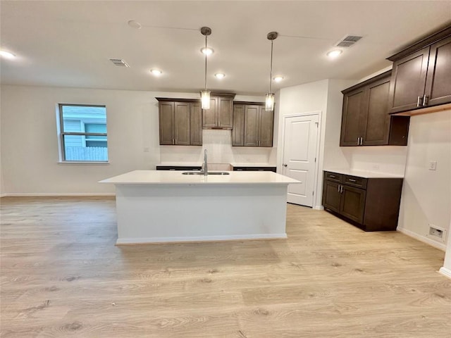 kitchen with a sink, light wood-style floors, dark brown cabinetry, a center island with sink, and recessed lighting
