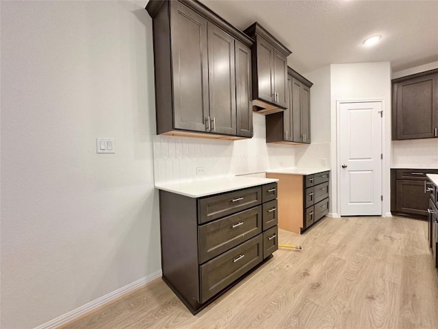 kitchen featuring light wood finished floors, baseboards, dark brown cabinets, and light countertops