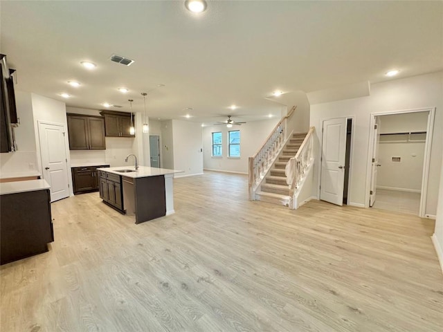 kitchen with a sink, open floor plan, dark brown cabinetry, baseboards, and light countertops
