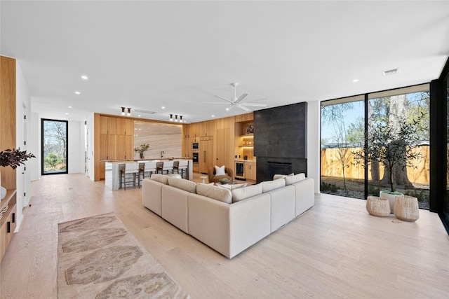 living area with light wood finished floors, recessed lighting, visible vents, expansive windows, and wooden walls