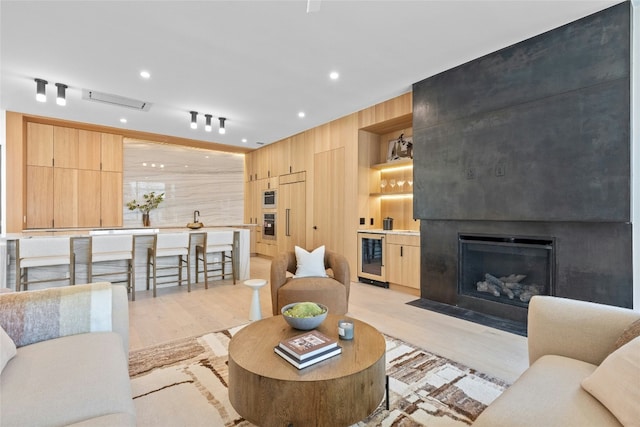 living room featuring a large fireplace, light wood finished floors, wine cooler, built in shelves, and recessed lighting