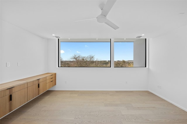 spare room featuring a ceiling fan, light wood-style flooring, visible vents, and a wealth of natural light