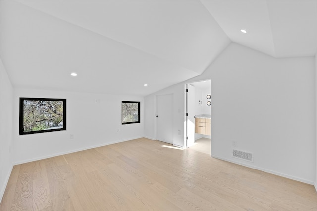 interior space featuring light wood-style floors, baseboards, visible vents, and vaulted ceiling