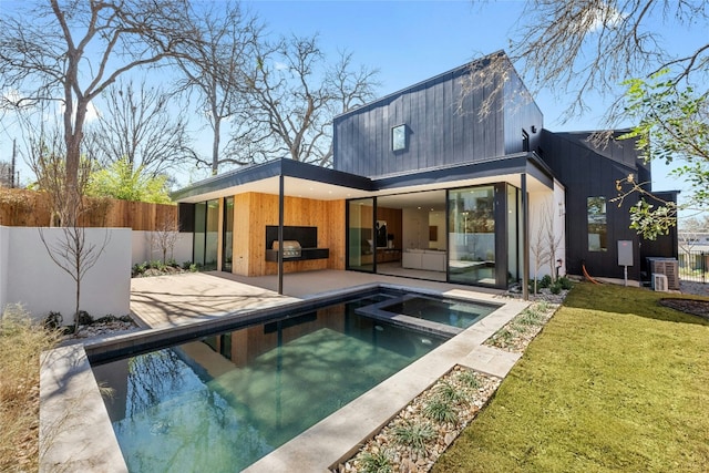 back of house featuring an outdoor kitchen, a lawn, an in ground hot tub, fence, and a patio area