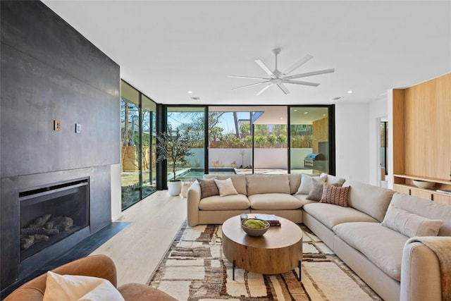 living room with a wall of windows, a fireplace, wood finished floors, and a ceiling fan