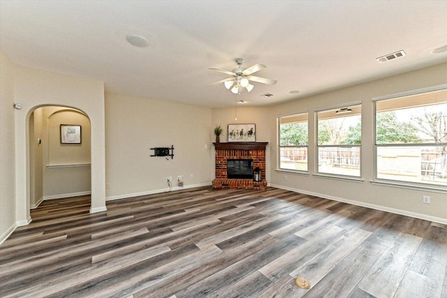 unfurnished living room with a brick fireplace, visible vents, arched walkways, and wood finished floors