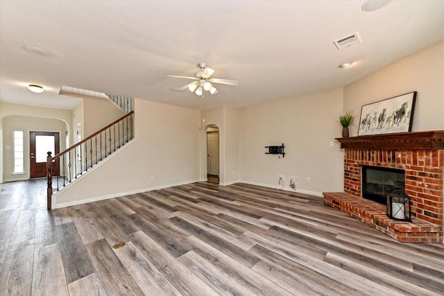 living area featuring arched walkways, wood finished floors, visible vents, stairs, and a brick fireplace