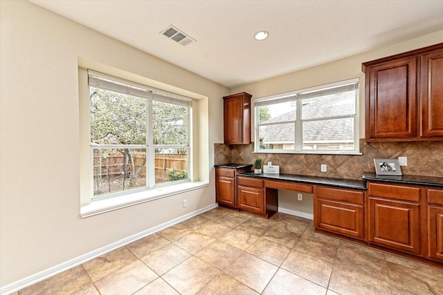 kitchen with dark countertops, visible vents, decorative backsplash, and built in desk