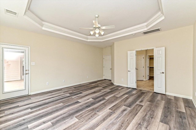 unfurnished bedroom with a tray ceiling, visible vents, baseboards, and wood finished floors