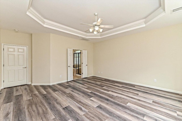 empty room with baseboards, visible vents, ornamental molding, wood finished floors, and a tray ceiling