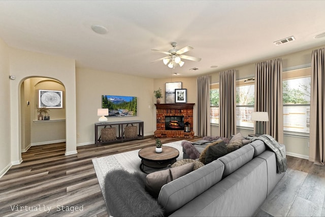 living area featuring arched walkways, a fireplace, wood finished floors, visible vents, and baseboards