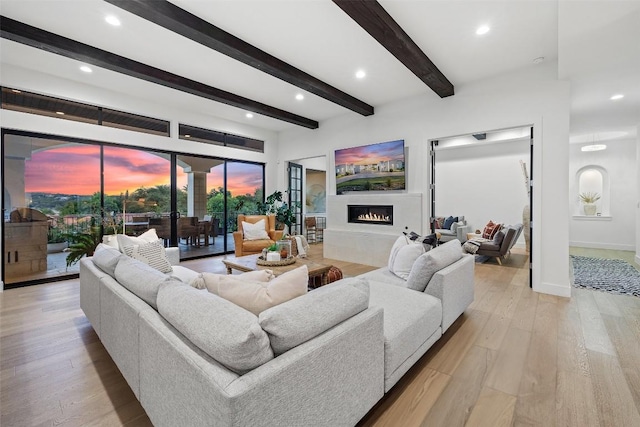 living room with beam ceiling, recessed lighting, light wood-type flooring, a warm lit fireplace, and baseboards