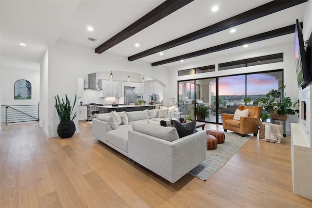 living area with arched walkways, light wood finished floors, beam ceiling, and visible vents