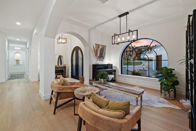 living area featuring arched walkways, a fireplace, light wood finished floors, recessed lighting, and baseboards