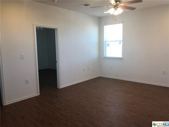 spare room featuring a ceiling fan, visible vents, dark wood finished floors, and baseboards