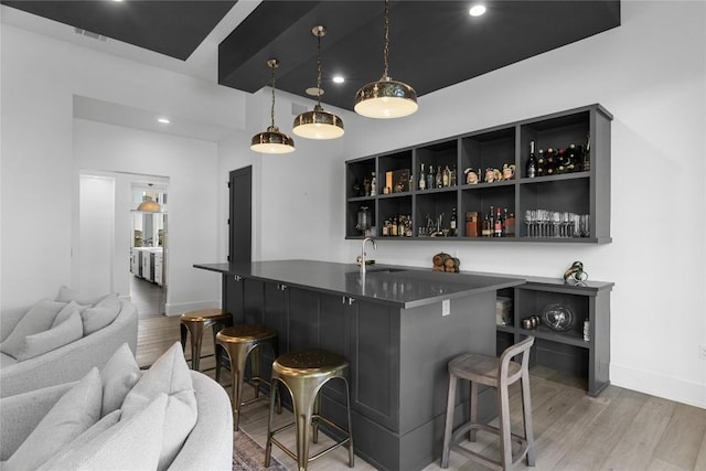 bar featuring light wood-type flooring, baseboards, a sink, and wet bar