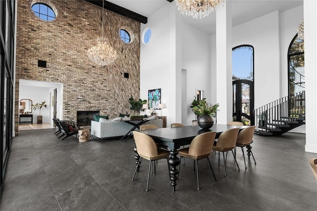 dining space with an inviting chandelier, a high ceiling, stairway, and a fireplace