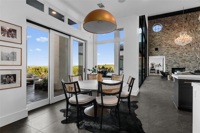 dining area with a notable chandelier, brick wall, a high ceiling, a fireplace, and visible vents