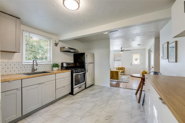 1908 E 21st St Unit 1And 2, Austin, TX 78722 - kitchen with appliances with stainless steel finishes, under cabinet range hood, wood counters, light marble finish floors, and tasteful backsplash
