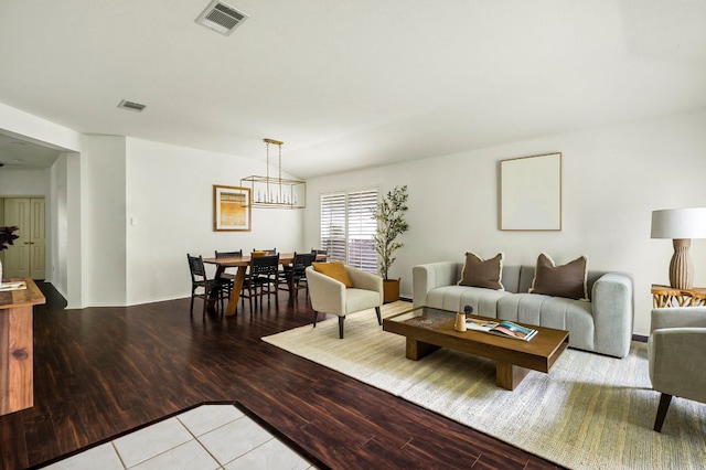 living room featuring baseboards, visible vents, light wood-type flooring, and an inviting chandelier
