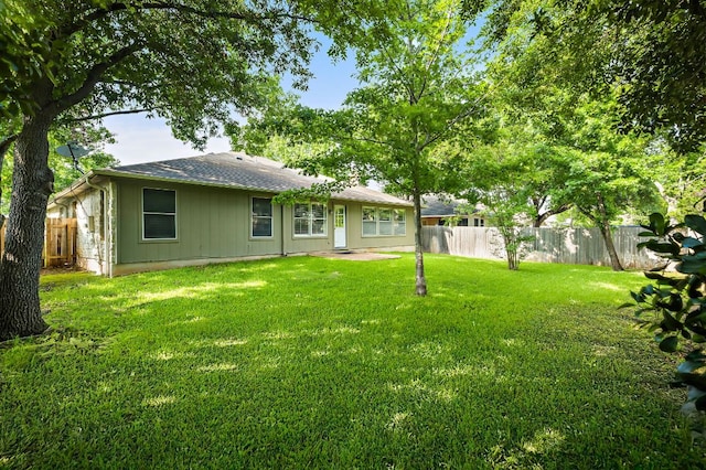 back of house with roof with shingles, a yard, and a fenced backyard