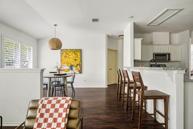 kitchen with stainless steel microwave, visible vents, baseboards, dark wood-style flooring, and a kitchen bar
