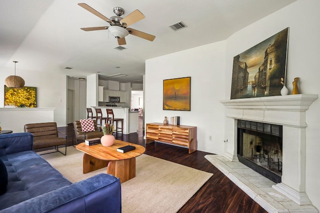 living room with visible vents, ceiling fan, a tiled fireplace, and wood finished floors