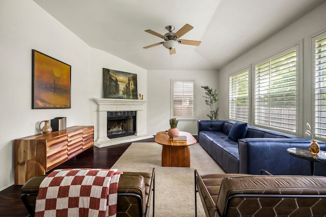 living area featuring a fireplace with raised hearth, ceiling fan, vaulted ceiling, baseboards, and wood finished floors