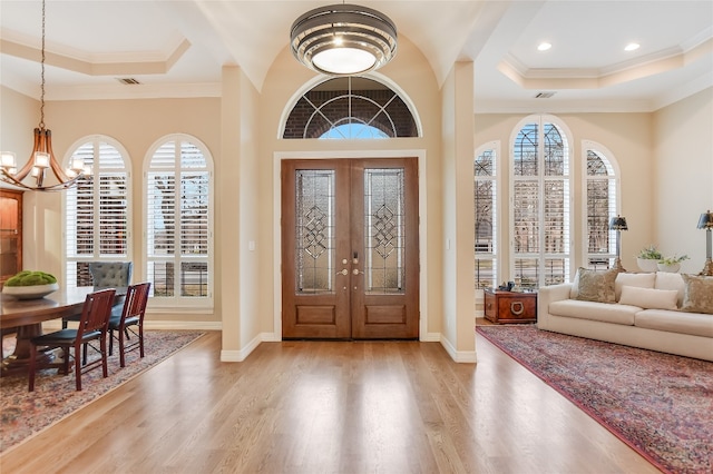 entryway with ornamental molding, a tray ceiling, wood finished floors, and an inviting chandelier