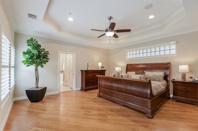 bedroom with visible vents, baseboards, a tray ceiling, light wood finished floors, and crown molding