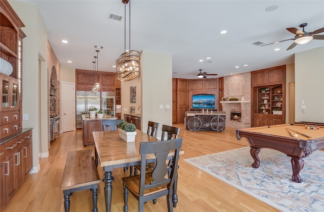 dining space with light wood-type flooring, a brick fireplace, visible vents, and recessed lighting