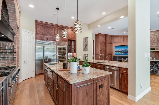 kitchen with a kitchen island with sink, premium range hood, a sink, light wood finished floors, and high end appliances