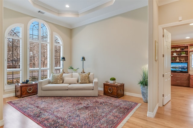 sitting room with a tray ceiling, light wood finished floors, visible vents, ornamental molding, and baseboards