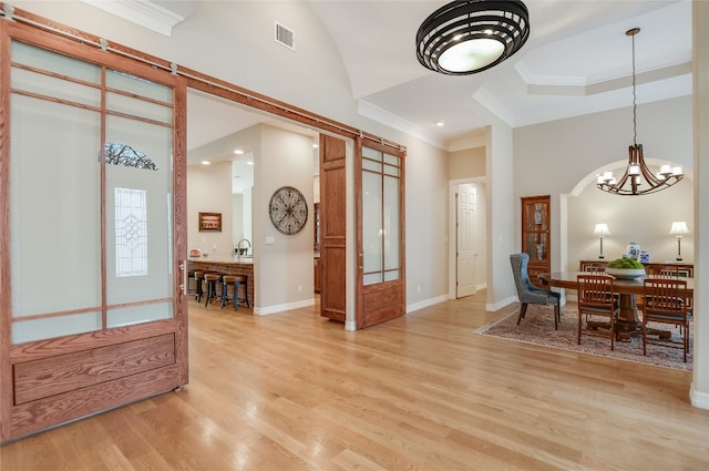 entryway featuring light wood-type flooring, a towering ceiling, visible vents, and crown molding