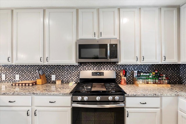 kitchen featuring stainless steel appliances, light stone countertops, white cabinetry, and tasteful backsplash