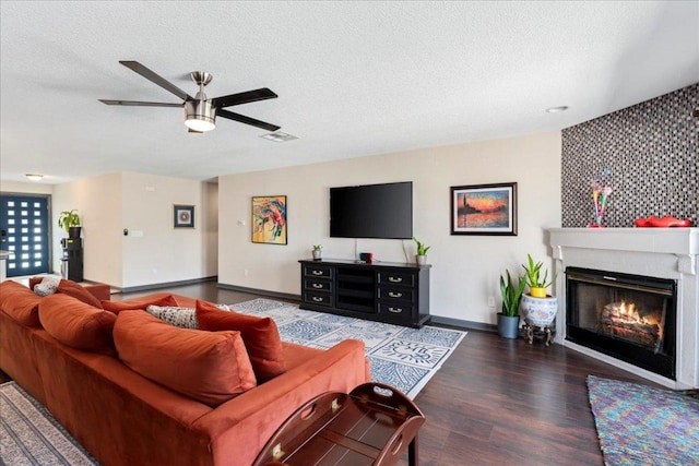 living area featuring a textured ceiling, wood finished floors, a ceiling fan, baseboards, and a glass covered fireplace