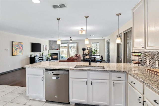 kitchen with a peninsula, a fireplace, a sink, visible vents, and stainless steel dishwasher