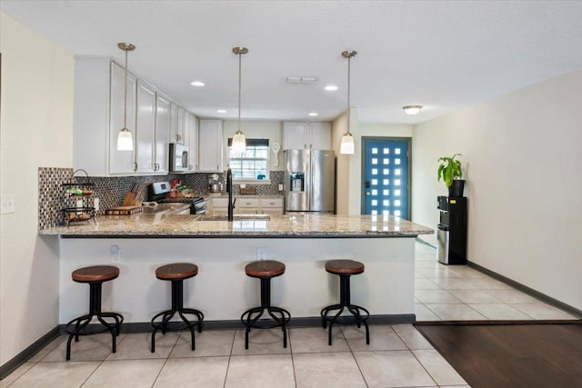 kitchen featuring light stone counters, appliances with stainless steel finishes, a peninsula, a sink, and backsplash