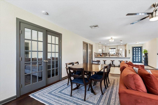 dining room with a textured ceiling, visible vents, baseboards, french doors, and dark wood finished floors