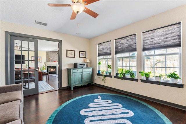 sitting room with baseboards, a lit fireplace, visible vents, and dark wood-type flooring