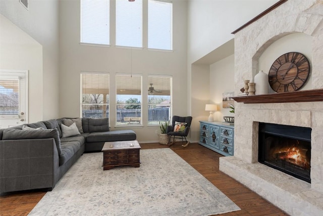 living room with a high ceiling, a premium fireplace, visible vents, baseboards, and dark wood finished floors