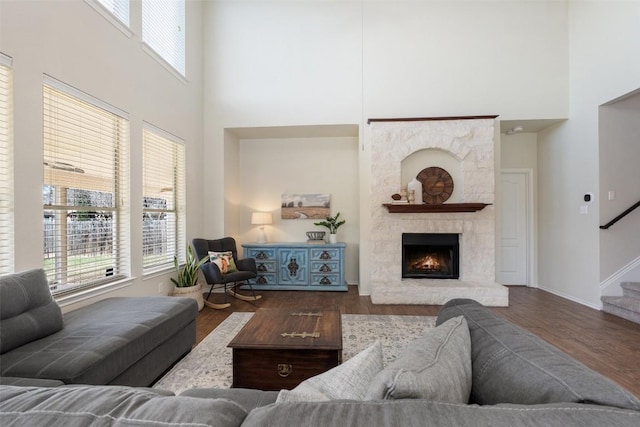 living area featuring stairs, a stone fireplace, wood finished floors, and a healthy amount of sunlight