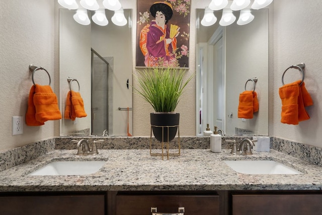 full bath with a textured wall, a sink, a shower stall, and double vanity