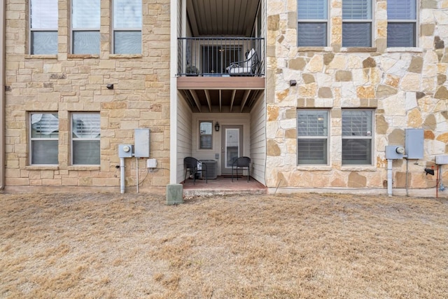 view of exterior entry with cooling unit, stone siding, a patio, and a balcony