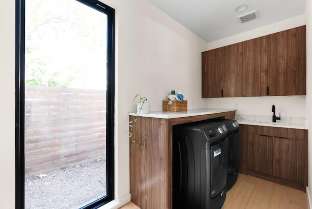 washroom featuring light wood-style flooring, a sink, visible vents, washer and dryer, and cabinet space