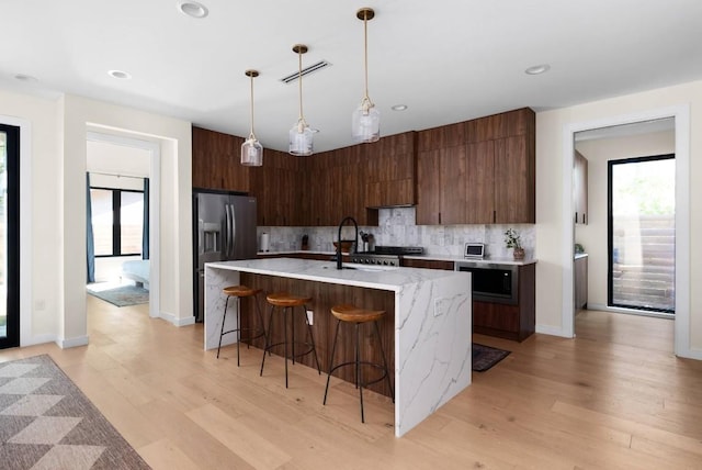 kitchen with visible vents, backsplash, built in microwave, plenty of natural light, and stainless steel fridge with ice dispenser