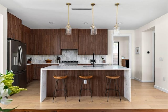 kitchen with a sink, light countertops, stainless steel refrigerator with ice dispenser, range, and modern cabinets