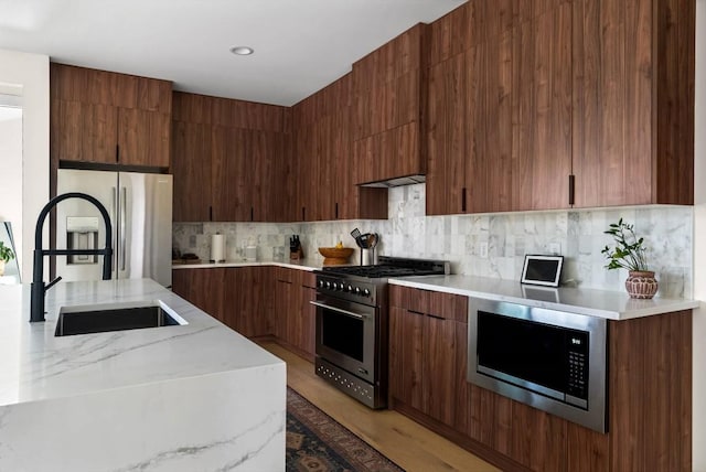 kitchen with light wood finished floors, modern cabinets, extractor fan, stainless steel appliances, and backsplash